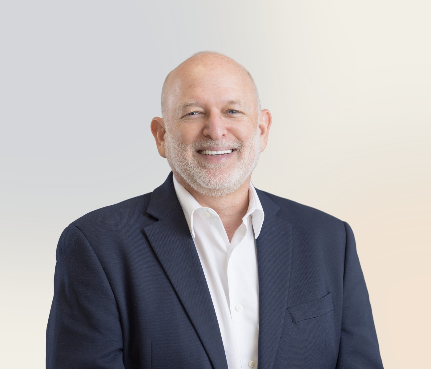 Evan Fuchs smiling in a navy jacket against a warm neutral background.